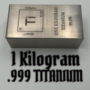 May include: A rectangular titanium bar with a brushed metallic finish. The top surface features an engraved periodic table element box for Ti, 22, 47.87, 4.54g/cc, 3034F, and text reading ONE KILOGRAM TITANIUM 99.5%. Below the bar, the text 1 KILOGRAM .999 TITANIUM.