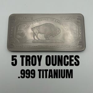 May include: A rectangular titanium bullion bar featuring an embossed American bison in the center. The text reads United States of America, 5 Five, Titanium Bullion, In God We Trust, and 5 Troy Ounce. The bar has a metallic gray finish.