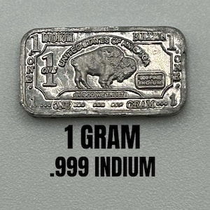 May include: A rectangular silver-colored indium bullion bar weighing 1 gram. The front features a buffalo, the text UNITED STATES OF AMERICA, IN GOD WE TRUST, 999 FINE INDIUM, and the number 1. The text 1 GRAM .999 INDIUM is printed below the bar.