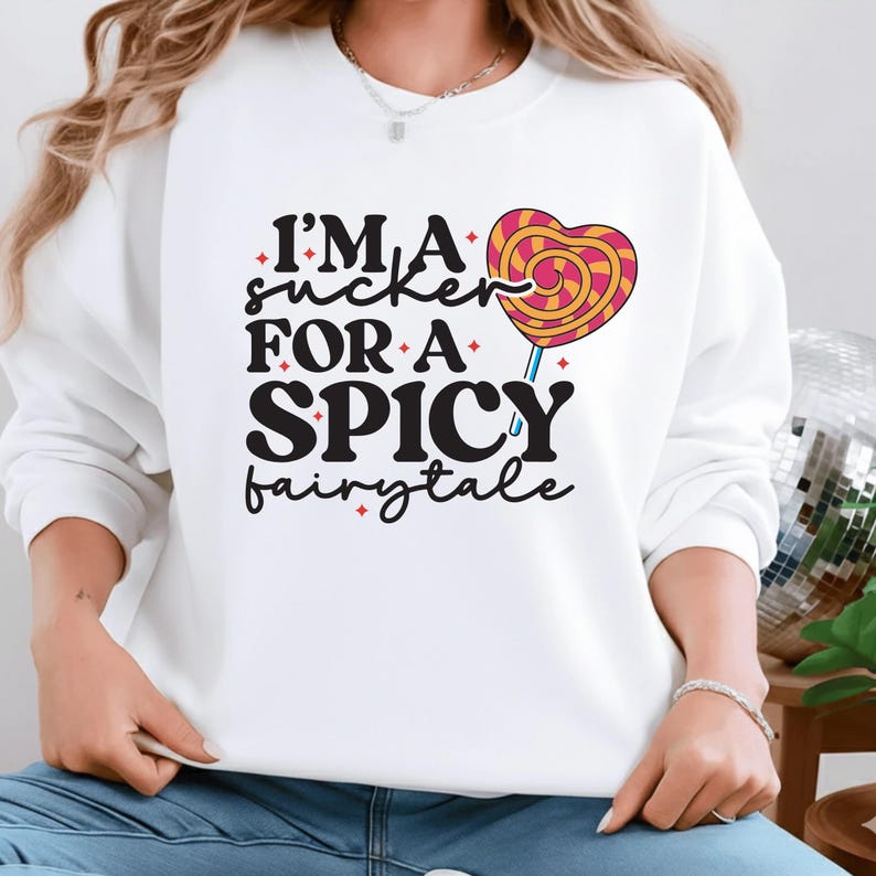 May include: White sweatshirt with the text "I'M A sucker FOR A SPICY fairytale" in black, with a heart-shaped lollipop graphic in pink, yellow, and orange. The sweatshirt is a casual style.
