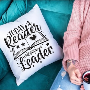 May include: White throw pillow with the text "Today a Reader Tomorrow a Leader" in black script. The design includes an open book with a heart and stars. The pillow is on a teal couch.