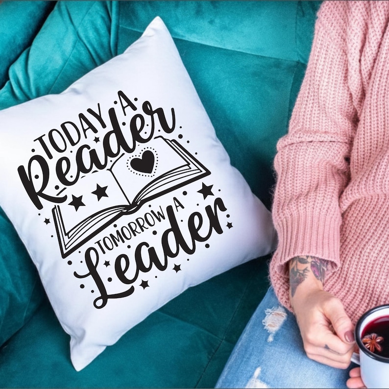 May include: White throw pillow with the text "Today a Reader Tomorrow a Leader" in black script. The design includes an open book with a heart and stars. The pillow is on a teal couch.