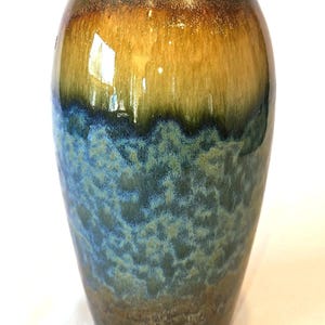May include: A cylindrical ceramic vase featuring a smooth, glossy glaze. The top section is a warm golden-brown, transitioning into a vibrant, mottled blue and teal midsection, and finishing with a dark, earthy brown base at the bottom.