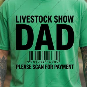 May include: A bright green short-sleeved t-shirt featuring the black text LIVESTOCK SHOW DAD, a barcode graphic, and the text 978123456789 PLEASE SCAN FOR PAYMENT printed on the front center of the garment in a bold, sans-serif typeface.