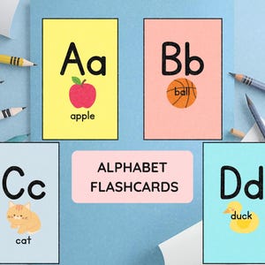 May include: Alphabet flashcards featuring the letters A through D. Each card has a letter, a corresponding image, and the word for the image. The cards are on a light blue surface with pencils.