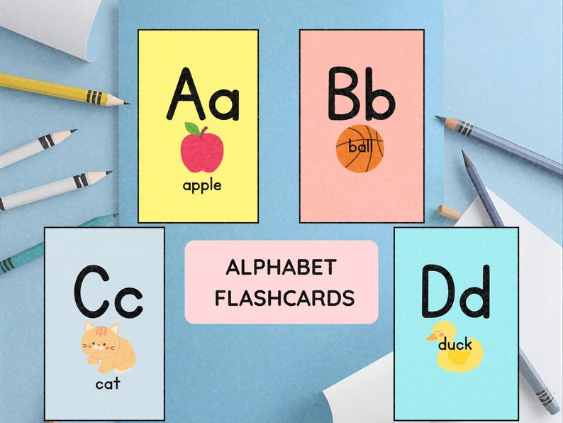 May include: Alphabet flashcards featuring the letters A through D. Each card has a letter, a corresponding image, and the word for the image. The cards are on a light blue surface with pencils.