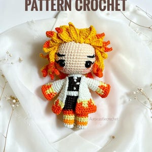 Puede incluir: Muñeca de ganchillo hecha a mano con cabello amarillo y naranja, que lleva un abrigo blanco con detalles en negro. La muñeca tiene una expresión neutra y está sobre un fondo blanco. El texto "PATTERN CROCHET" se muestra encima de la muñeca.