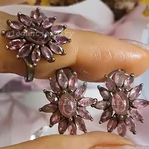 Könnte beinhalten: Ein Schmuckset mit einem Ring und einem Paar Ohrringen. Jedes Stück zeigt ein Blumenmuster mit mehreren rosa Edelsteinen. Der Ring und die Ohrringe sind vor einem weichen Hintergrund platziert, der die Details hervorhebt.