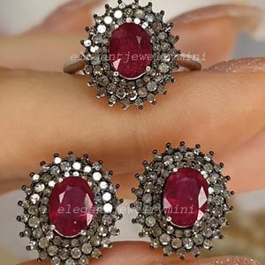 Pode incluir: Um conjunto de joias com um anel e brincos. Cada peça tem um rubi oval central rodeado por um halo de pedras claras menores. O anel e os brincos são cravejados em metal prateado. O texto "elegant jewelry mini" é visível.