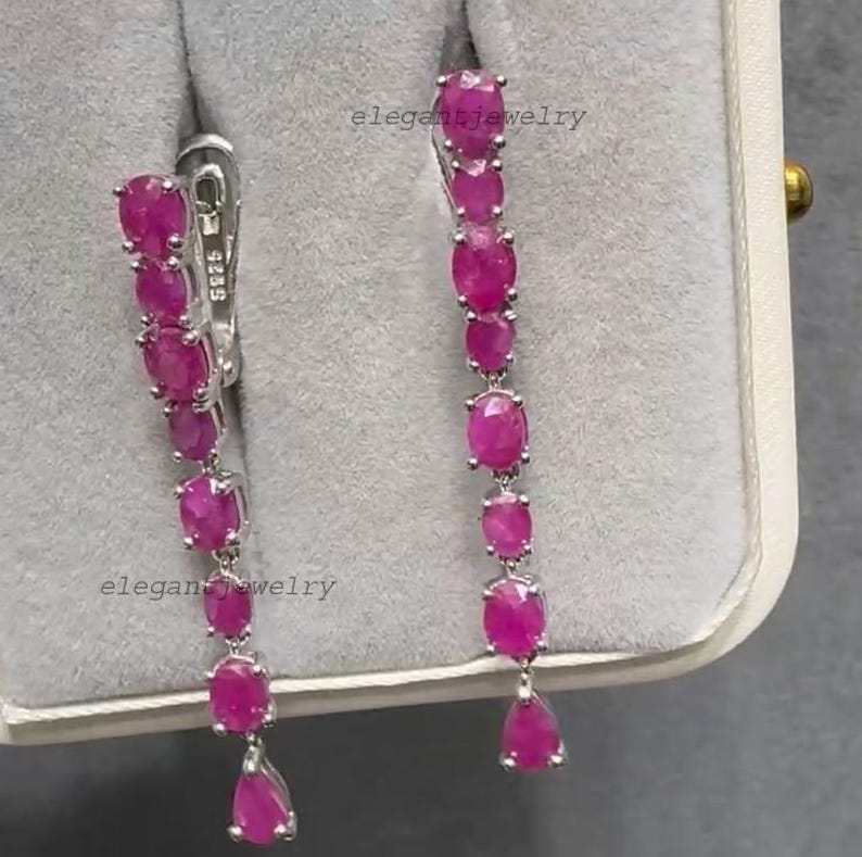 Pu&ograve; includere: Un paio di eleganti orecchini pendenti con una cascata di pietre preziose rosa vivaci di forma ovale e a goccia. Gli orecchini sono incastonati in metallo argentato, con chiusura a gancio. Il testo "elegantjewelry" &egrave; visibile.