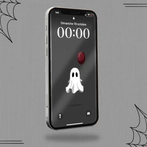 May include: A smartphone displays a Halloween-themed wallpaper. The screen shows a white ghost with a red balloon against a dark gray background. The time reads 00:00, and the date is displayed as Dimanche 19 octobre.