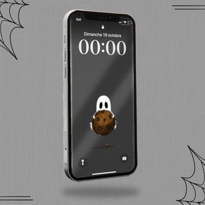 Peut inclure: Un smartphone affiche un fond d'écran sur le thème d'Halloween. L'écran de verrouillage montre un fantôme de dessin animé tenant un cookie, avec l'heure 00:00 et la date "Dimanche 19 octobre" en blanc. Le téléphone est sur un fond gris avec des toiles d'araignées.
