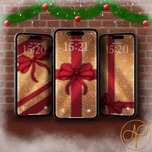 Peut inclure: Trois smartphones affichent des fonds d'écran sur le thème de Noël. Chaque écran présente un fond doré avec des rubans et des nœuds rouges, et l'heure 15h20 ou 15h21. Une guirlande avec des boules rouges décore le haut.