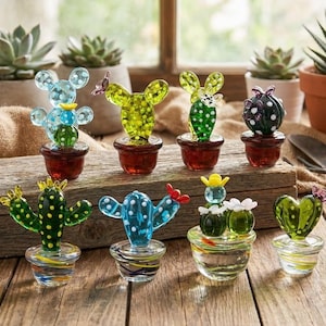 May include: A collection of colorful glass cactus sculptures in various shapes and sizes. The cacti are in small pots and bowls, with details like polka dots and butterfly accents. The colors include green, blue, and yellow, set against a rustic wooden surface.