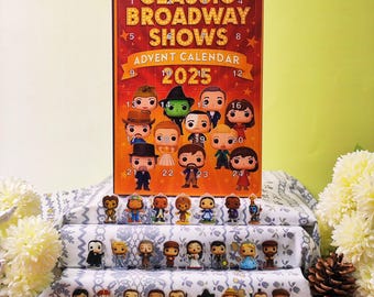 May include: A Classic Broadway Shows Advent Calendar for 2025, featuring miniature figurines of characters from various musicals. The calendar is red with gold lettering and star accents. The figurines are arranged on a patterned fabric.
