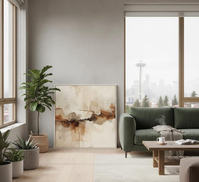 May include: A square framed wall art piece featuring an abstract landscape painting with layered washes of cream, beige, and deep brown tones. The artwork is displayed in a thin light-colored frame, showcasing fluid, organic shapes and textures.