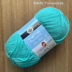 May include: A large ball of dark turquoise yarn with a label that reads "Snuggly Wuggly Douce Accolade Abrazo Dulce". The yarn is a vibrant teal color, perfect for knitting or crocheting projects. The label features a baby and the words "Free Gratuit".