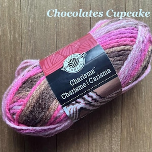 May include: A skein of Loops & Threads Charisma yarn in the colorway Chocolates Cupcake. The yarn is a blend of pink, brown, and cream colors. The label reads "Charisma" and "Carisma".