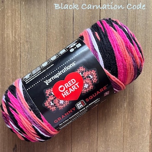 May include: A skein of Red Heart Granny Square yarn in the Black Carnation colorway. The yarn is a mix of black, pink, white, and purple. The label reads "Yarnspirations" and "Red Heart".