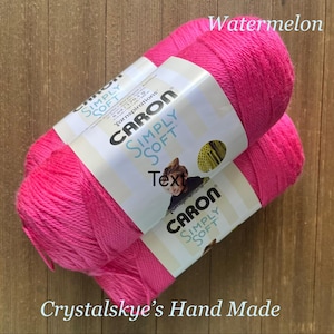 May include: Two skeins of Caron Simply Soft yarn in a vibrant watermelon pink. The labels read "Caron Simply Soft" and "Yarnspirations". The text "Crystalskye's Hand Made" is at the bottom.