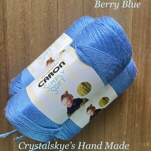 May include: Two skeins of Caron Simply Soft yarn in Berry Blue. The yarn is a soft, light blue color. The labels feature a child and the text "Crystalskye's Hand Made".