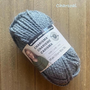 May include: A skein of charcoal gray Charisma yarn, 3.5 oz, with a label showing the brand name and a woman wearing a knitted shawl. The label also indicates 109 yards of yarn. The word "Charcoal" is written in cursive.