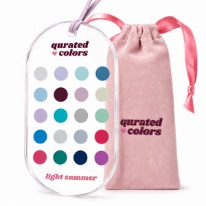 Könnte beinhalten: Ein ovaler, durchsichtiger Acrylanhänger mit dem Text "qurated colors" und "light summer" sowie einem Raster aus zwanzig farbigen Kreisen. Ein hellviolettes Band ist oben befestigt. Daneben liegt ein rosa Samtbeutel mit demselben Text.