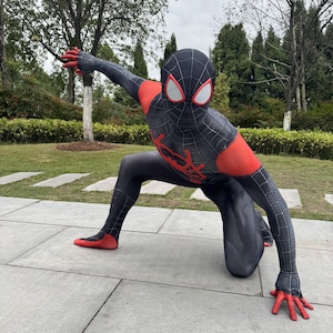 May include: A black and red Spider-Man costume with a web pattern. The costume features a mask with white eye lenses and red accents on the arms, hands, and feet. The character is kneeling on a stone surface.
