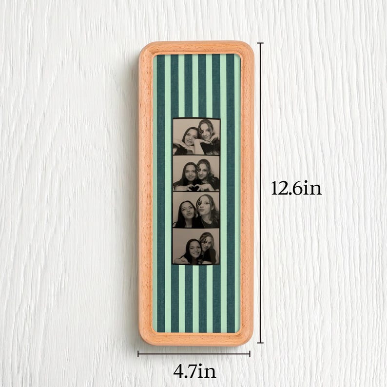 Puede incluir: Un marco de madera rectangular que contiene una tira vertical de cuatro fotos en blanco y negro de dos personas. El fondo detr&aacute;s de las fotos tiene rayas verticales de color verde oscuro y verde claro. Las dimensiones son 32cm por 12cm.