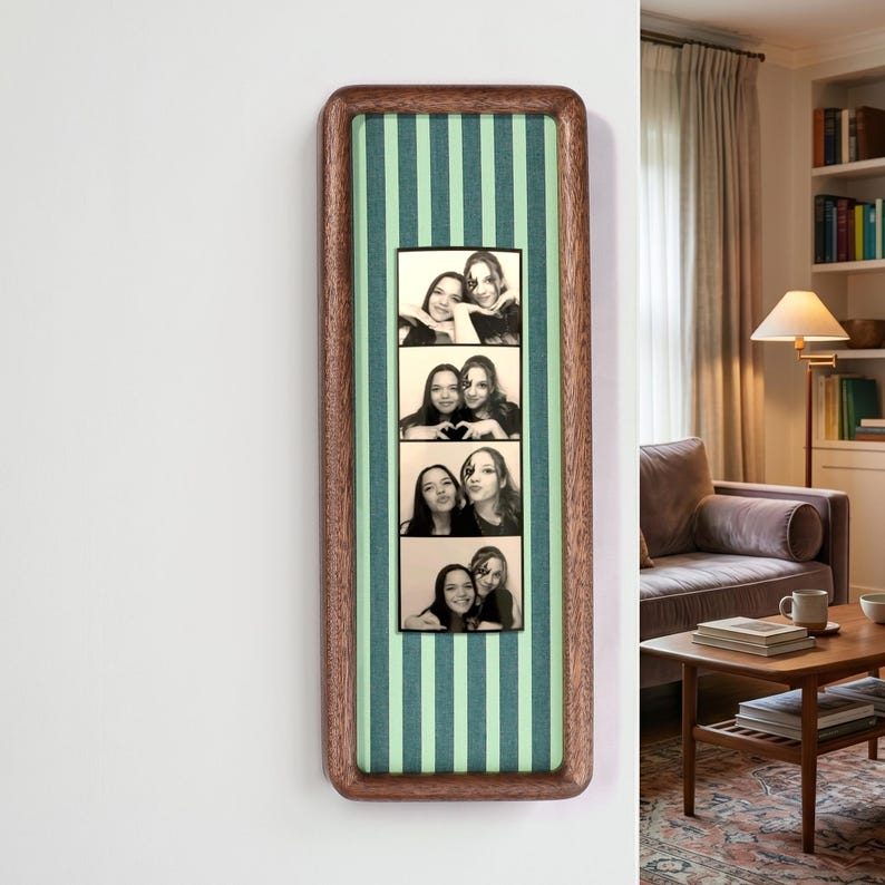 Puede incluir: Un marco de madera rectangular vertical con esquinas redondeadas, que presenta un fondo de tela a rayas de color verde claro y verde oscuro. Centrada en el interior hay una tira de fotos en blanco y negro que muestra cuatro poses de dos personas.