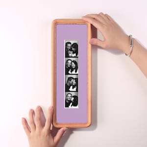 May include: A rectangular wooden picture frame with rounded corners, featuring a light purple mount. Inside the frame is a vertical strip of four black and white photographs showing a couple in various poses, displayed against a white background.