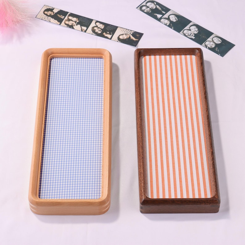 Puede incluir: Dos bandejas rectangulares de madera con esquinas redondeadas. La bandeja izquierda es de madera clara con una base de patr&oacute;n de cuadros vichy azul y blanco. La derecha es de madera oscura con rayas verticales naranjas y blancas. Dos tiras de fotos arriba.