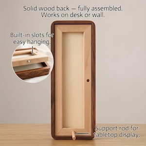 Puede incluir: Un marco de exhibici&oacute;n rectangular de madera con un borde exterior de nogal oscuro y un panel interior de madera de haya clara. Incluye una varilla de soporte para mesa, ranuras integradas para colgar y el texto: Solid wood back&mdash;fully assembled.