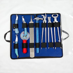 Puede incluir: Un kit de herramientas azul con varias herramientas de herrador de metal. Las herramientas incluyen cuchillos para cascos, una lima, un martillo, tenazas y un abrebotellas. Los mangos son azules y el kit está contenido en una funda azul.