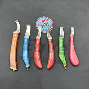 Puede incluir: Seis cuchillos para cascos con hojas curvas de acero inoxidable y mangos de madera coloridos. Los mangos son marrones, azules, rojos, verdes y rosas. Los cuchillos están dispuestos sobre una superficie gris oscuro, con un logotipo circular en el fondo.