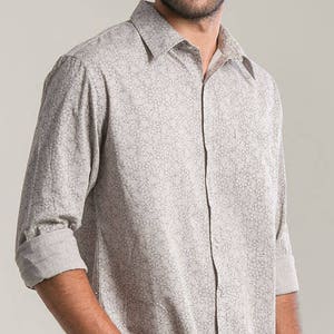 Puede incluir: Una camisa de manga larga con botones y un diseño estampado en gris claro y blanco.
