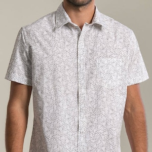 Puede incluir: Una camisa blanca de manga corta con botones y un patrón geométrico negro.