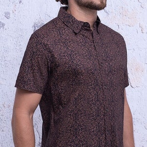 May include: A brown short-sleeved button-down shirt with a dark brown abstract pattern.