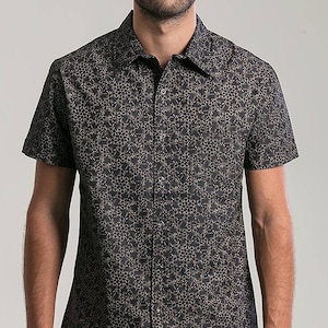 May include: A short-sleeved button-down shirt with a black background and a repeating gold floral pattern. The shirt has a classic collar and is worn by a person. The shirt is made of a lightweight fabric.