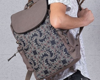 May include: A brown canvas backpack with a flap closure and a black and red patterned front panel. The backpack has a zippered pocket on the front and adjustable straps.