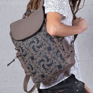 May include: A brown canvas backpack with a flap closure and a black and red patterned front panel. The backpack has a zippered pocket on the front and adjustable straps.