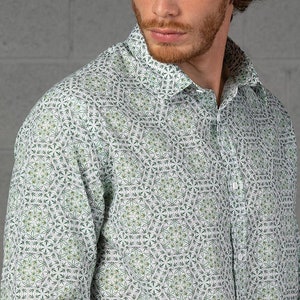 Pode incluir: Uma camisa branca de manga comprida com botões e um padrão de folhas verdes. A camisa tem uma gola clássica e um fecho de botões na frente.