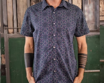 Peut inclure: Une chemise à manches courtes boutonnée bleu foncé avec un motif géométrique de petits points blancs et violets. La chemise a un col et une fermeture boutonnée.