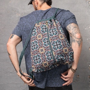 May include: A green drawstring backpack with a colorful geometric pattern. The backpack has a zipper closure and adjustable straps.