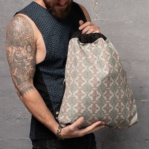 May include: A drawstring bag with a geometric pattern in shades of pink, green, and beige. The bag is made of a soft, textured fabric and has a black drawstring.