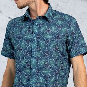 Puede incluir: Una camisa de manga corta con botones y un patrón geométrico azul verdoso y azul. La camisa tiene cuello y cierre de botones en la parte delantera.
