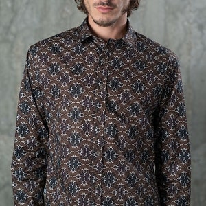 May include: A button-down shirt with a repeating pattern in brown, white, and navy blue. The long-sleeved shirt has a classic collar and is made of a soft, likely woven fabric. The shirt is worn by a person.