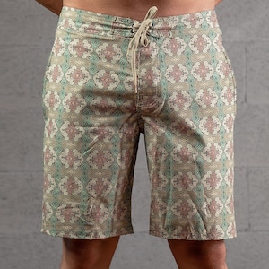 May include: Beige swim trunks with a geometric pattern in shades of green, brown, and pink.