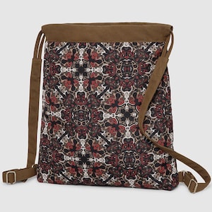 May include: A patterned shoulder bag with brown straps and trim. The bag's main body displays a repeating design in red, black, and beige. The straps are adjustable, and the bag has a rectangular shape. The bag's dimensions are not visible.