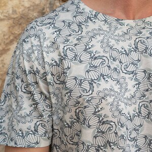 May include: A short-sleeved shirt with a white background and a black and green pattern. The pattern is a repeating design of interlocking circles and lines.